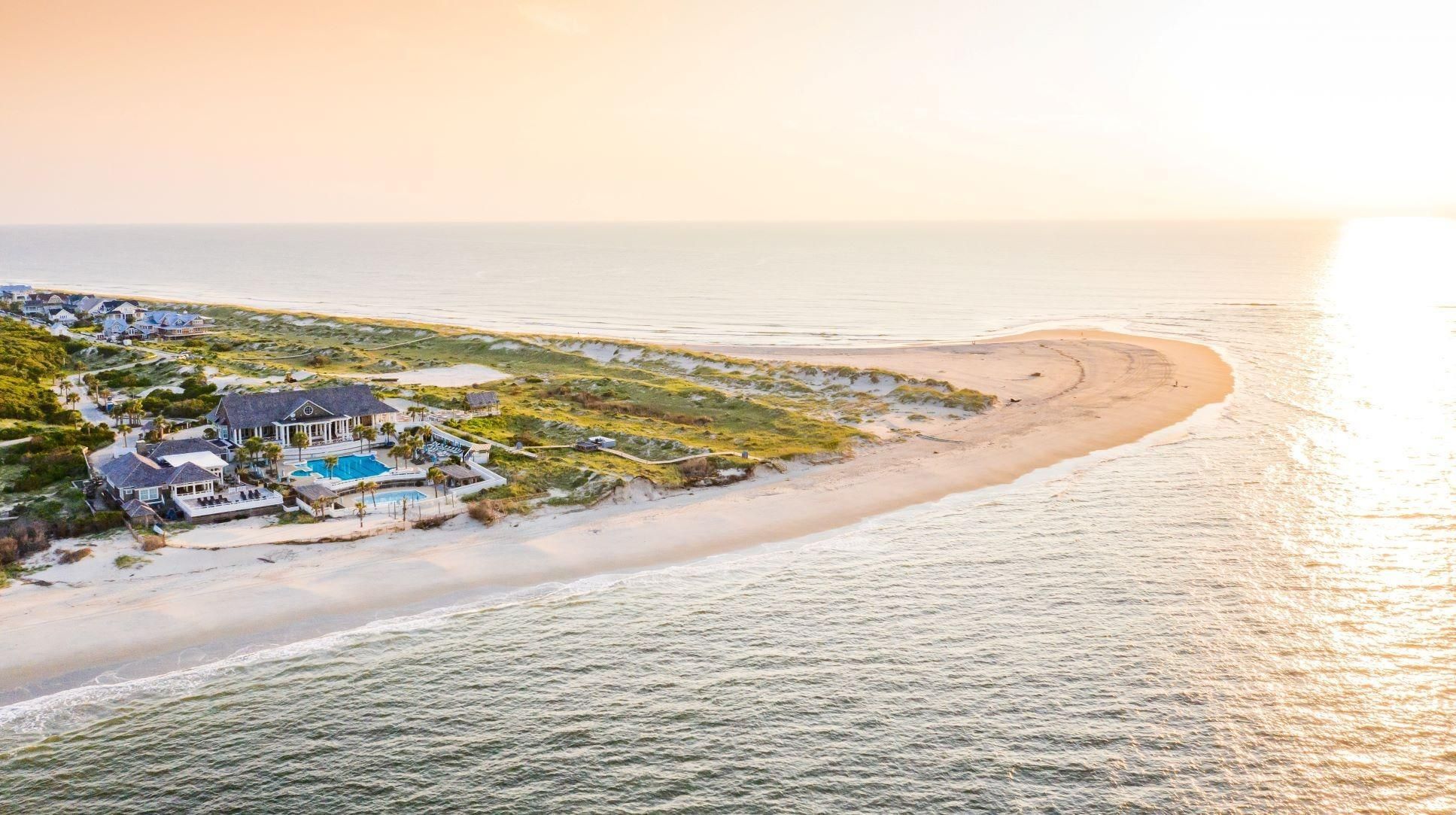 Luxurious beachfront mansion with a pool, situated on a sandy peninsula with the ocean on both sides.