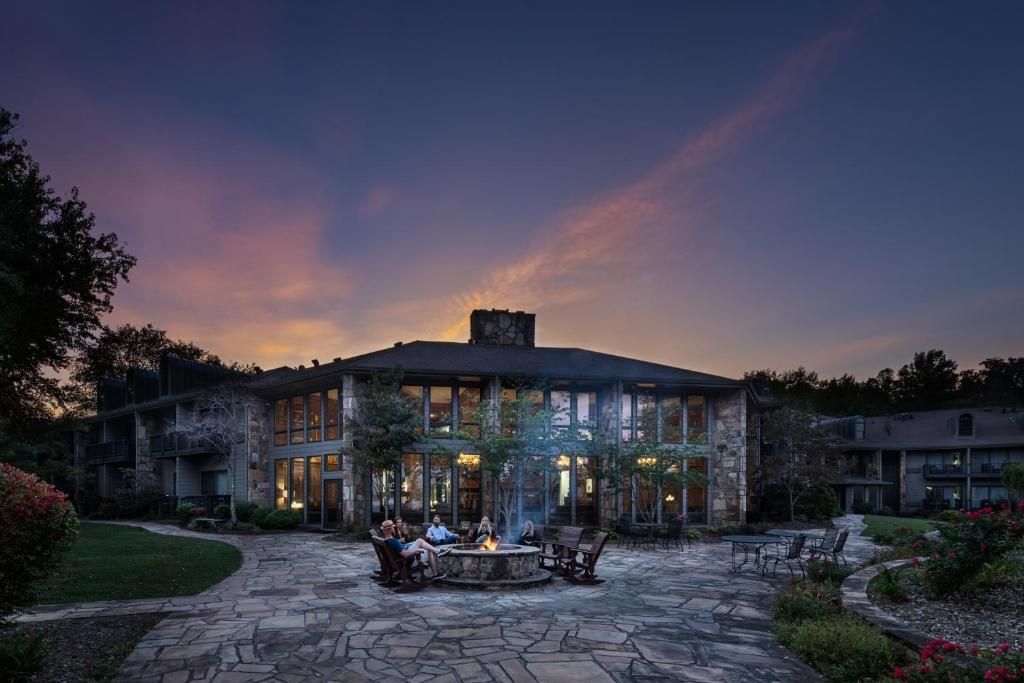 A large stone mansion with a glowing fire pit in the foreground at dusk.