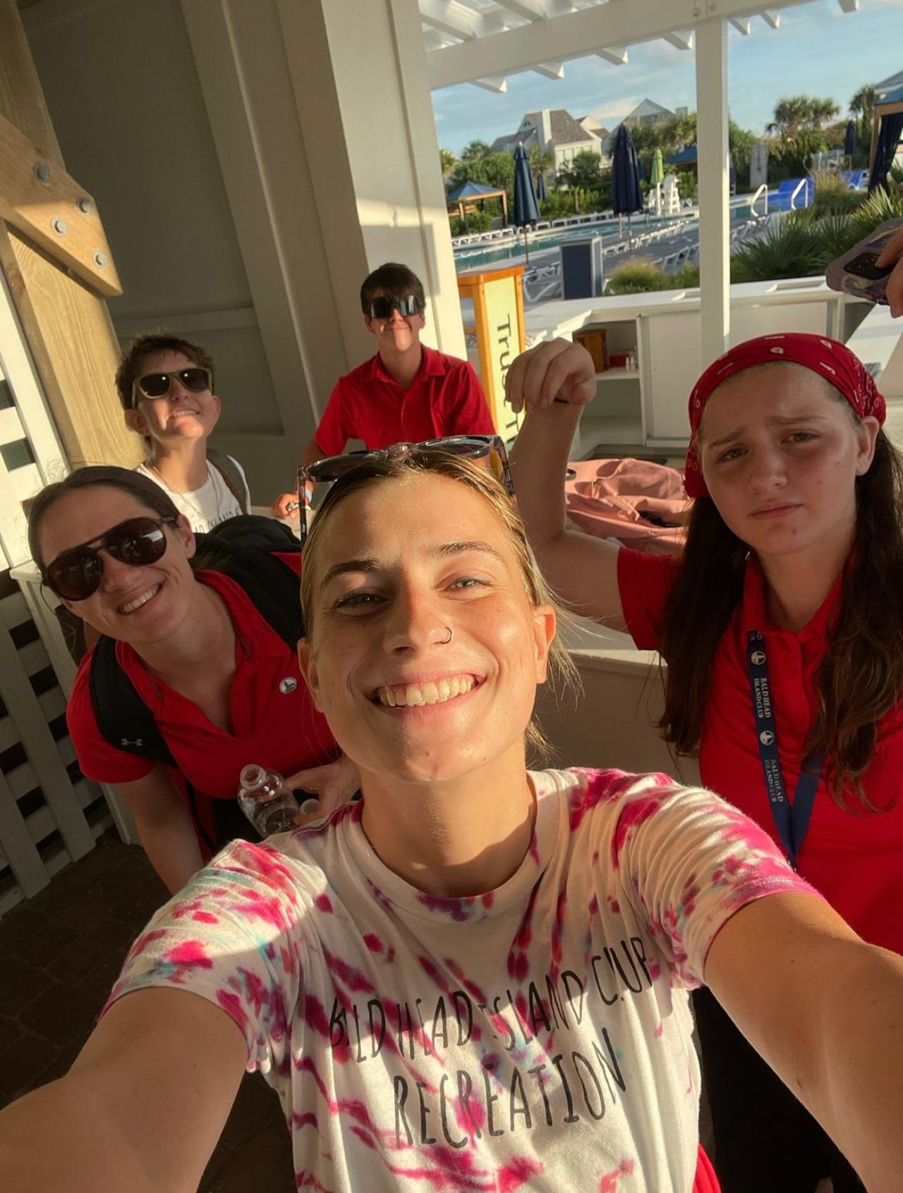 A group of five young people in red shirts smile for a selfie outdoors.