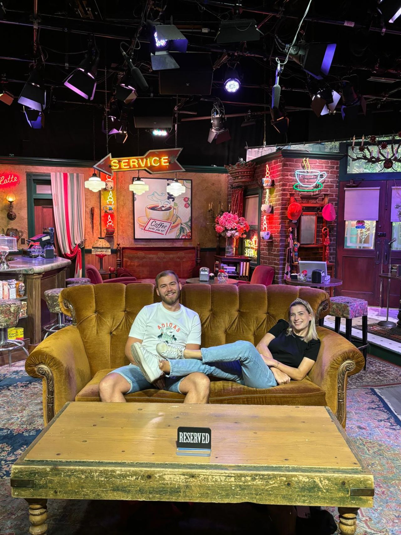 Two people relax on the iconic orange couch from the TV show Friends set.