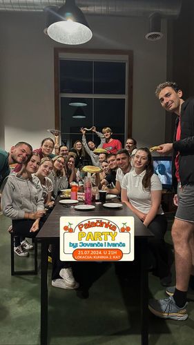 A group of young adults poses for a photo around a long table laden with food and drinks.