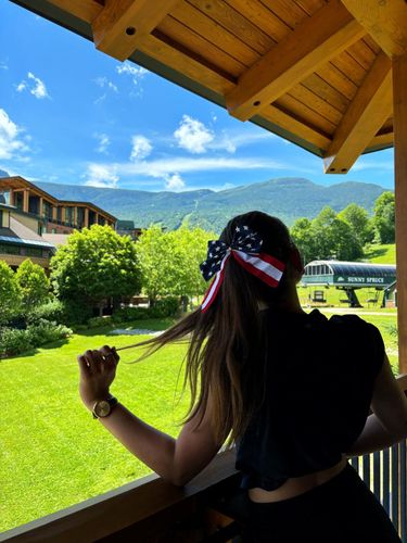 Woman wearing a bandana looks out at a green valley with mountains.