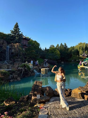 A young woman in a white crop top and sparkly pants poses by a waterfall and turquoise pool.