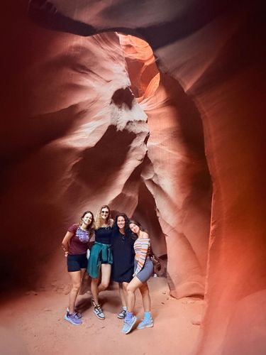 A group of five people pose for a photo inside a narrow, sculpted sandstone canyon with warm, glowing light.
