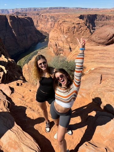 Two young women pose for a photo at Horseshoe Bend with the Colorado River in the background.