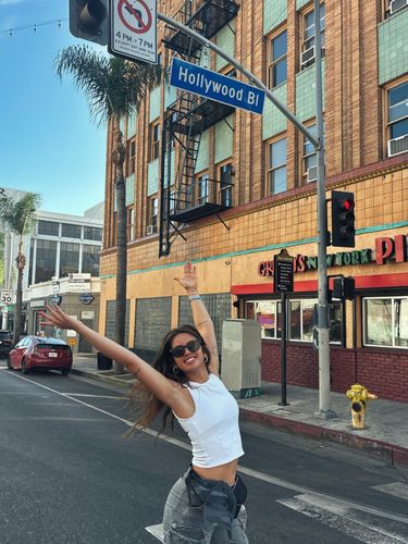 A woman poses with arms outstretched in front of a Hollywood street sign.