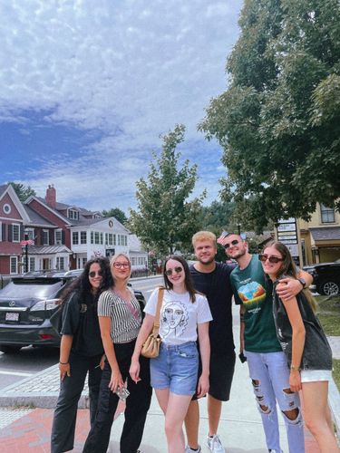 Group of six young adults smiling and posing for a photo outdoors on a sunny day.