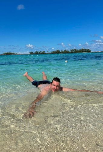 Man floating on his back in shallow, clear turquoise ocean water with arms and legs spread.
