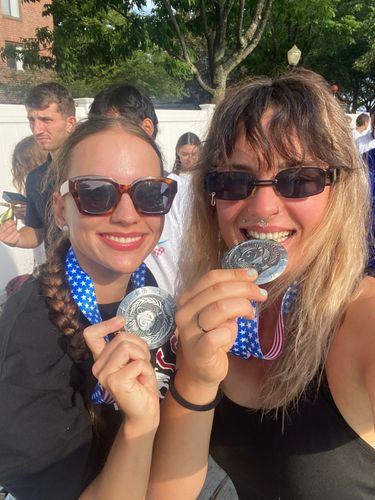 Two smiling women with medals around their necks, holding them up to the camera.