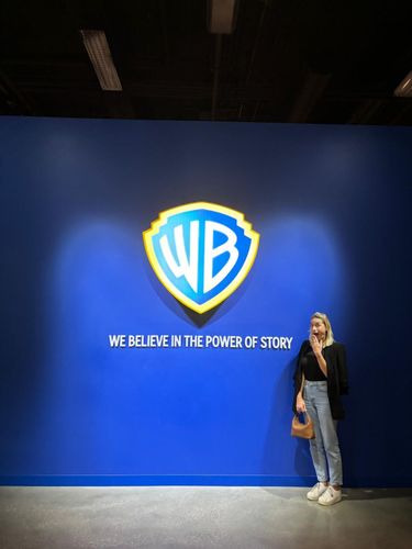 Woman stands in front of a large blue wall with the iconic Warner Bros. shield logo and the tagline 