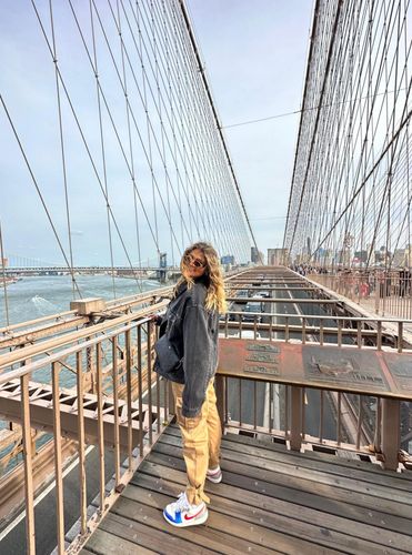 A person stands on the wooden walkway of the Brooklyn Bridge, looking out at the city skyline.